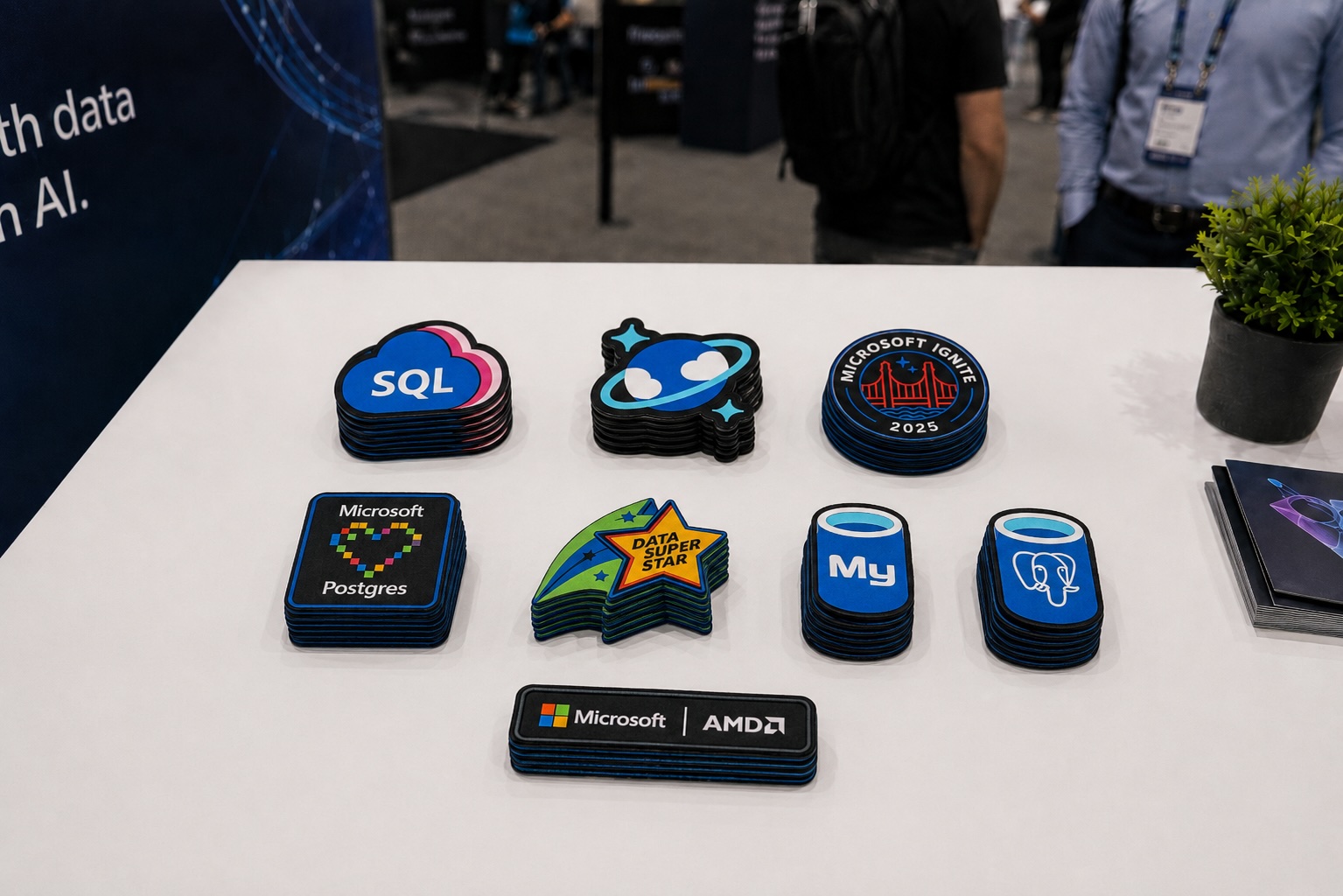 Eight stacks of embroidered Azure database patches on a white booth table, including SQL, Cosmos DB, Postgres, and Microsoft Ignite 2025 designs.